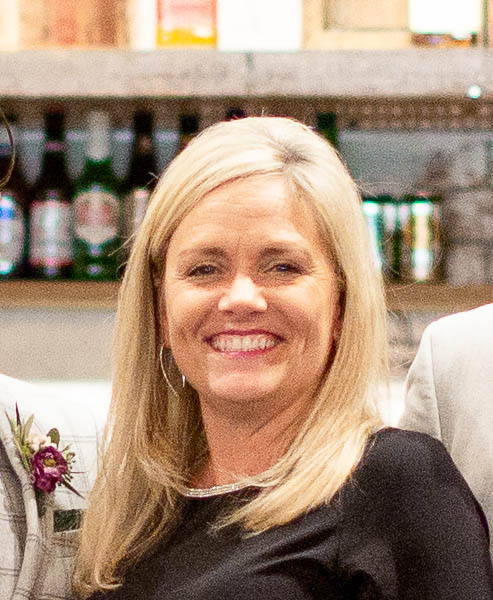 A woman wearing black and smiling with bottles in the background